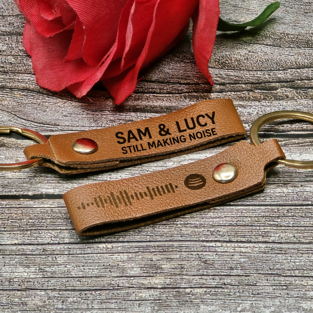 Tan PU leather keyrings with gold rings and snap fasteners. One strap is engraved SAM & LUCY and STILL MAKING NOISE, the other with a Spotify code